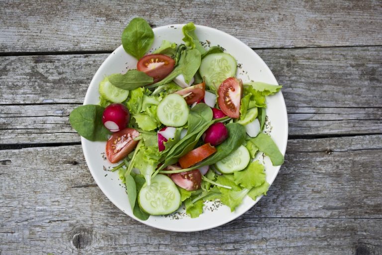Auf einem Untergrund aus Holz steht ein weißer Teller, appetitlich angerichtet, mit Salatblättern, Tomaten, Gurken und Radieschen